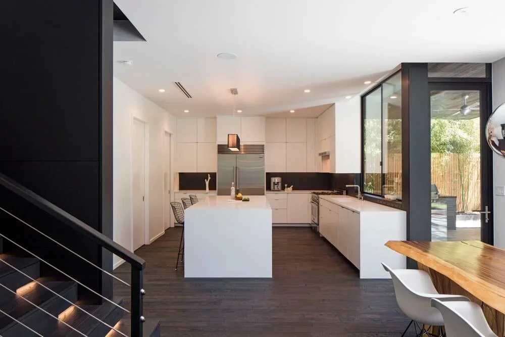 Open white kitchen with a waterfall island, dark backsplash, and stairs leading down to the dining area