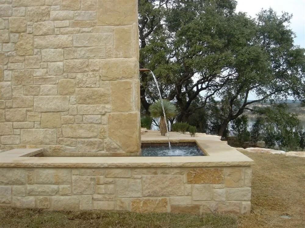 Limestone fountain basin bubbling beside a stone wall, with an oak and distant lake view