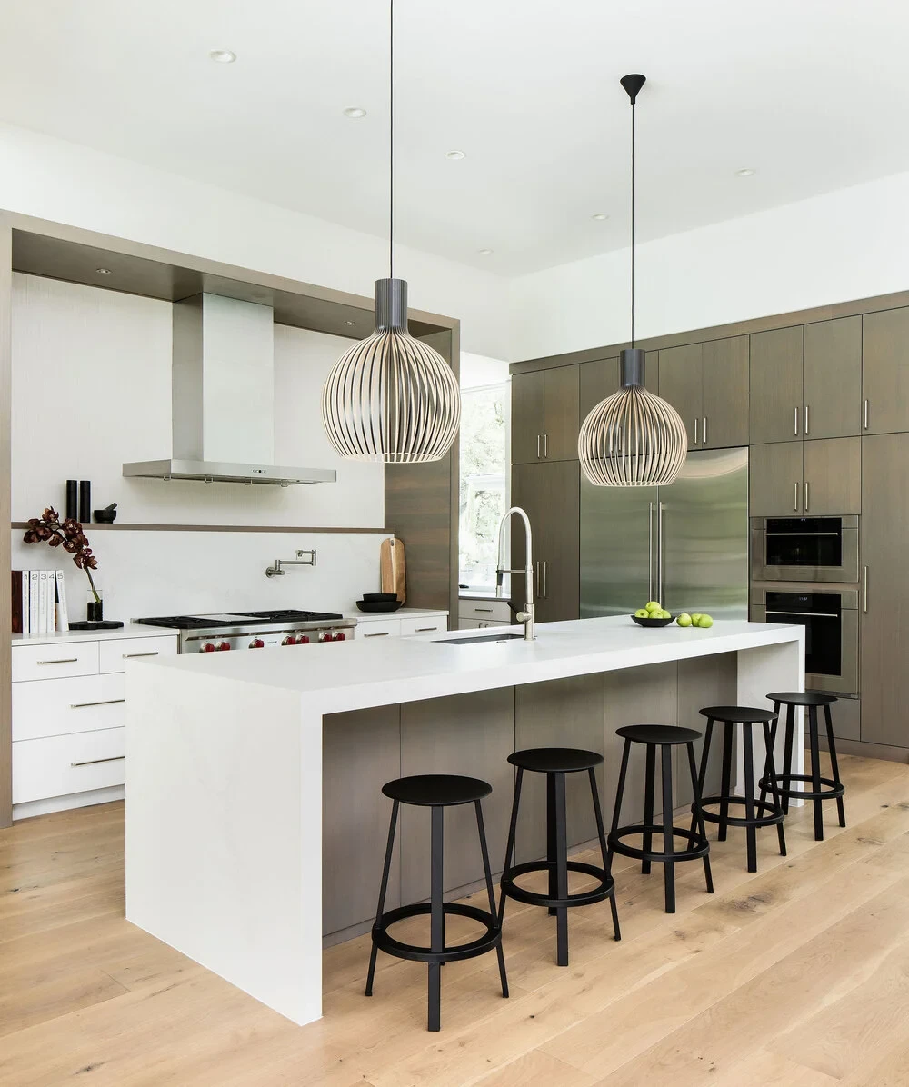 Modern kitchen with a white waterfall island, black stools and sculptural wood pendant lights