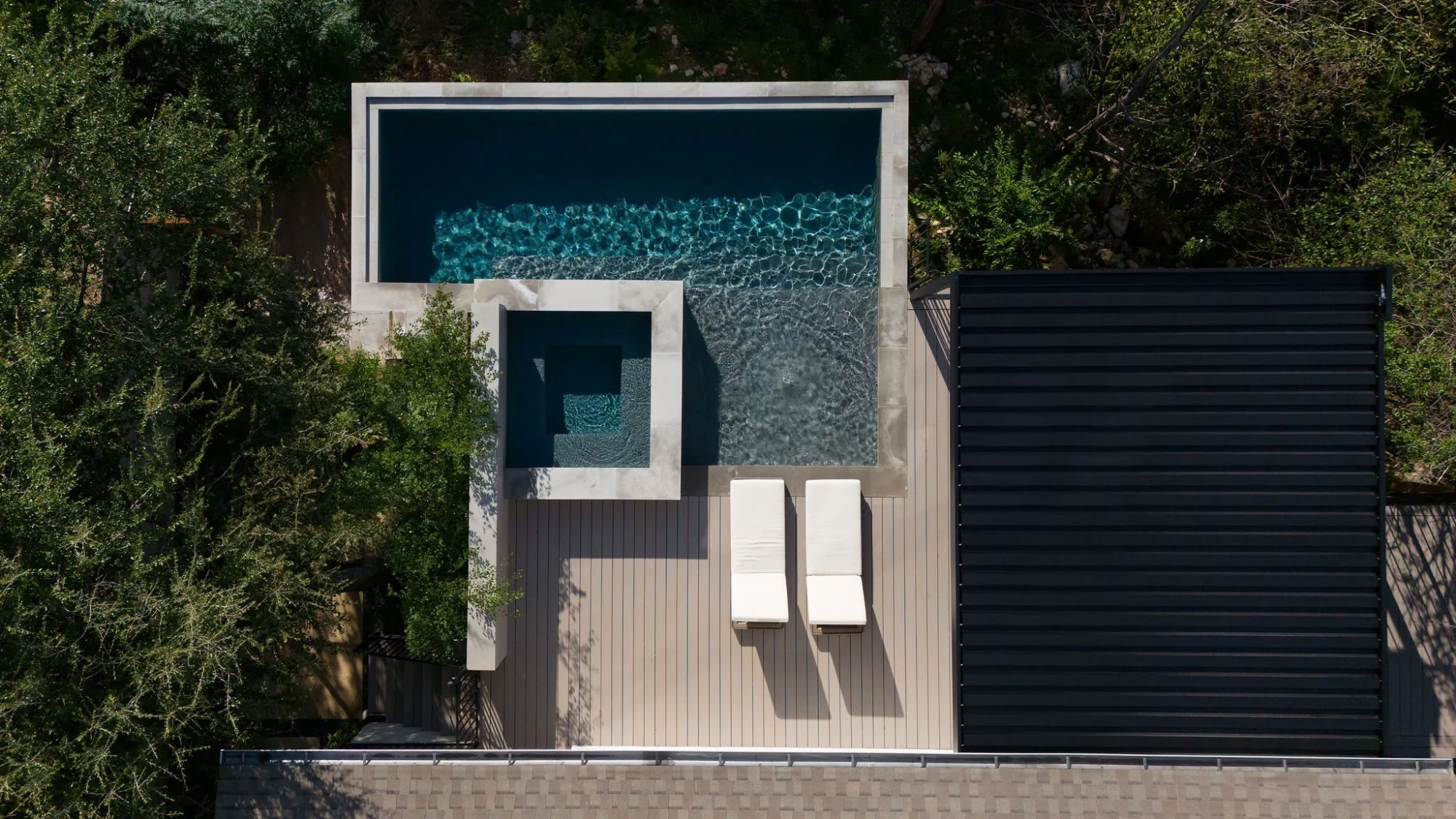 Overhead view of an L-shaped infinity pool and spa with loungers, deck, and oaks in Rollingwood