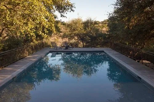 Geometric pool reflecting oaks and a wood deck, ringed by woods on a Hill Country slope