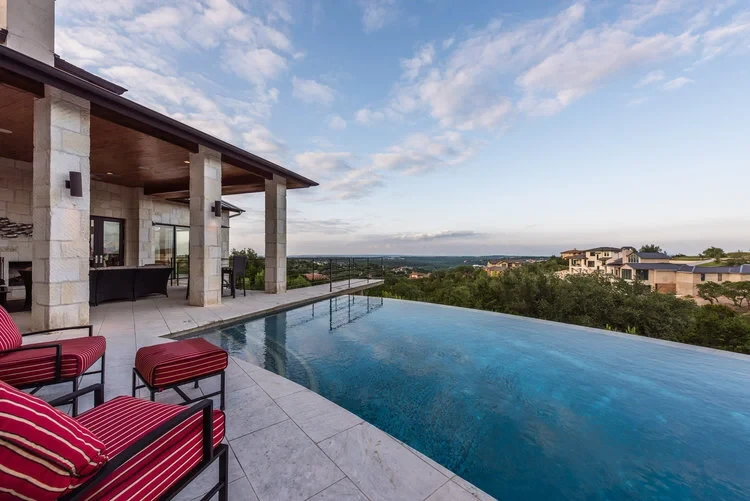 Infinity pool stretching toward the Hill Country horizon beside a covered stone patio with red loungers