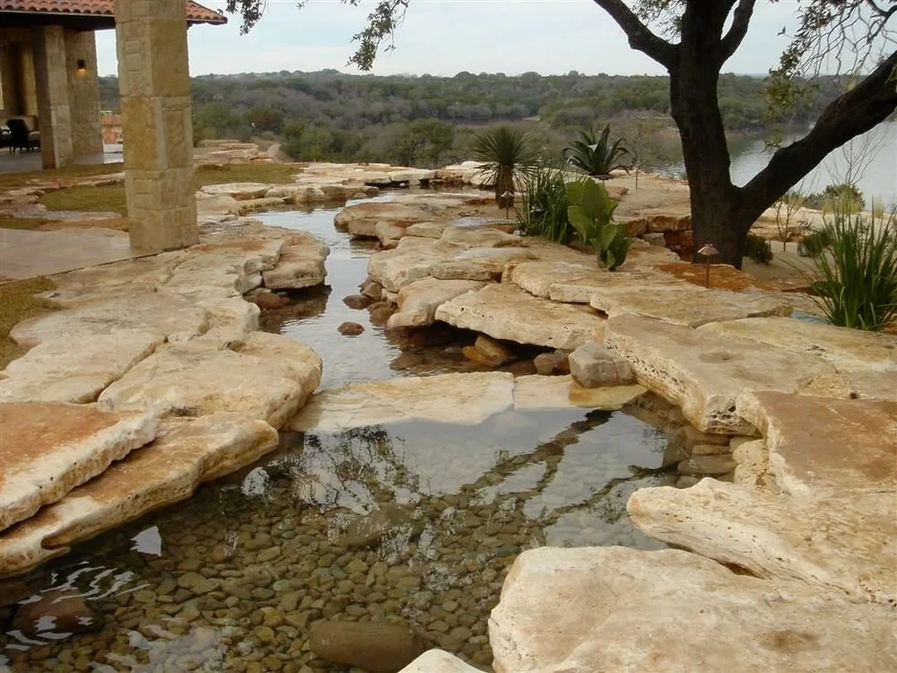 Shallow stone creek threading through flat limestone slabs across a Hill Country yard