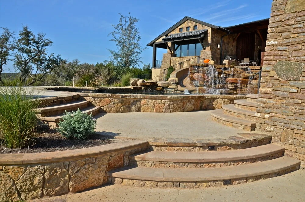 Tiered flagstone steps and retaining walls leading up to a stone Hill Country home with covered porch